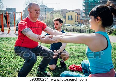 Picture - Calisthenics class at outdoor gym, instructor supporting man and woman practicing yoga. Fotosearch
