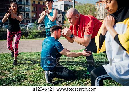 Stock Image - Calisthenics class at outdoor gym, trainer supporting man and women practicing yoga position. Fotosearch