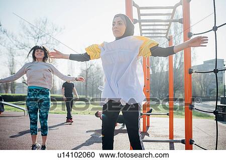 Stock Image - Calisthenics class at outdoor gym, young women jumping with arms outstretched. Fotosearch