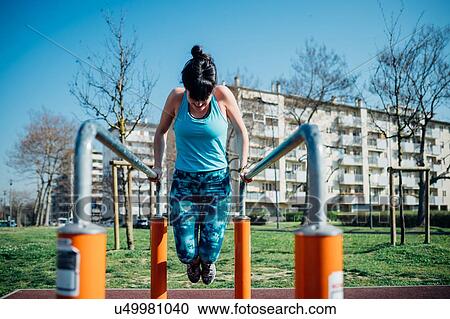 Stock Image - Calisthenics class at outdoor gym, young woman doing push ups on parallel bars. Fotosearch