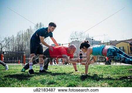 Stock Photo - Calisthenics class at outdoor gym, instructor supporting man and woman practicing yoga. Fotosearch
