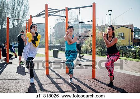 Stock Photograph - Calisthenics class at outdoor gym, young women balancing on one leg. Fotosearch