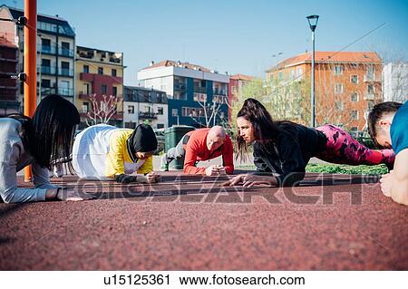 Stock Image - Calisthenics class in park, males and females doing push ups. Fotosearch