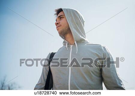 Stock Image - Calisthenics in park, young man in hoody against blue sky. Fotosearch