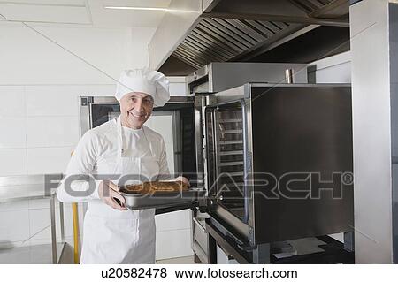Chef holding meat in roasting tray by oven View Large Photo Image Stock Photo - Chef holding meat in roasting tray by oven. Fotosearch