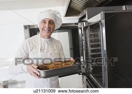 Stock Photo - Chef holding meat in roasting tray by oven. Fotosearch
