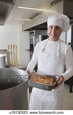 Stock Image - Chef holding meat in roasting tray. Fotosearch
