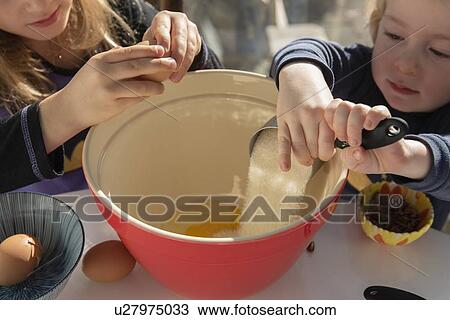Stock Image - Children pouring ingredients into bowl. Fotosearch