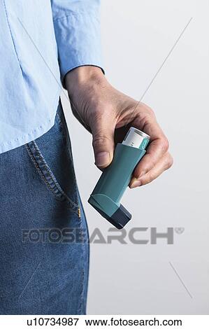 Stock Photo - Close-up of hand holding an asthma inhaler. The inhaler contains bronchodilator drugs, which widen constricted airways in the lungs.. Fotosearch