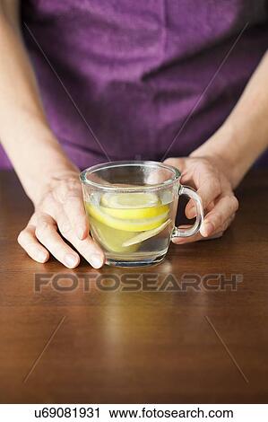 Stock Image - Close-up of hands holding lemon and ginger tea.. Fotosearch