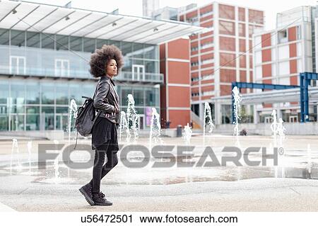 Stock Image - Cool young woman with afro hair on city concourse, full length. Fotosearch