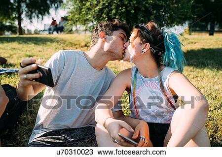 Couple kissing, using smartphone in park View Large Photo Image Stock Image - Couple kissing, using smartphone in park. Fotosearch