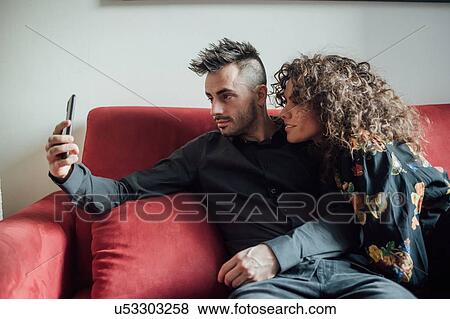 Stock Photo - Couple taking selfie on sofa. Fotosearch