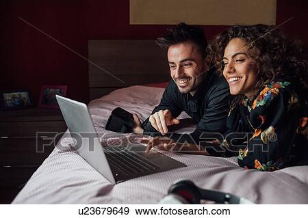 Stock Photo - Couple using laptop on bed. Fotosearch