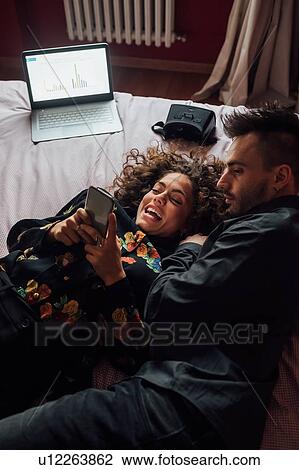 Stock Image - Couple using smartphone on bed. Fotosearch