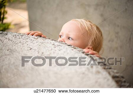 Stock Image - Cute female toddler peering over wall. Fotosearch