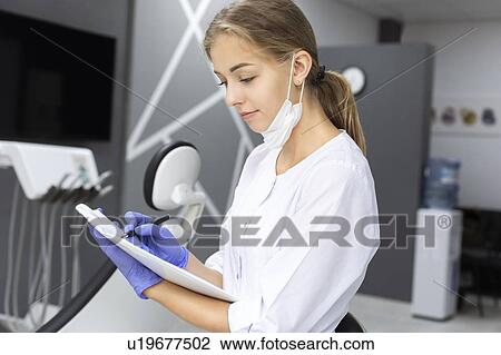 Stock Image - Dental assistant writing notes. Fotosearch