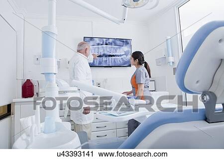 Stock Image - Dentist and dental hygienist examining X-ray on television screen. Fotosearch