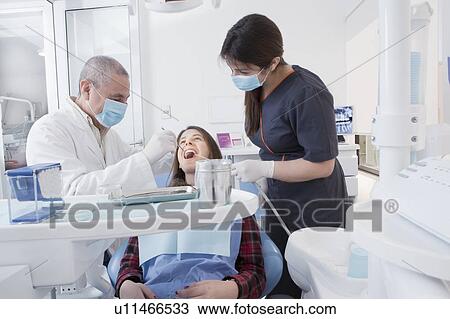 Stock Image - Dentist and hygienist cleaning patient's teeth. Fotosearch