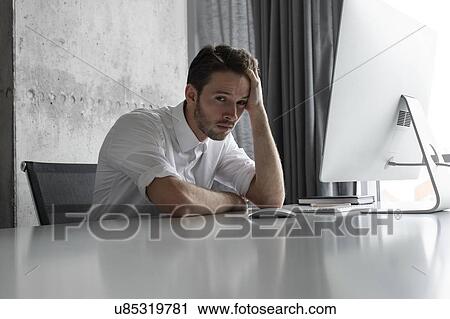 Stock Image - Depressed businessman sitting at desk. Fotosearch