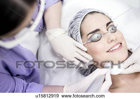 Stock Photo - Dermatologist using carbon dioxide laser resurfacing machine on woman's face, close-up. This treatment is used on acne scars, wrinkles, skin pigmentation, warts, and spots.. Fotosearch
