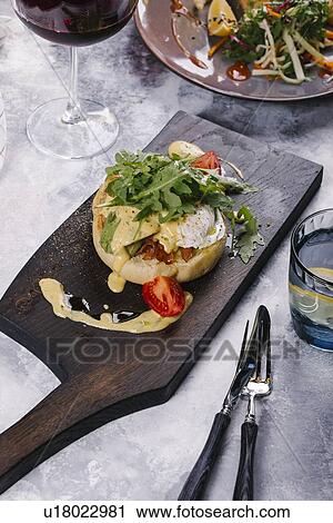 Stock Image - Eggs Benedict served on wooden cutting board. Fotosearch