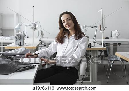 Stock Image - Fashion designer sitting at desk in studio. Fotosearch