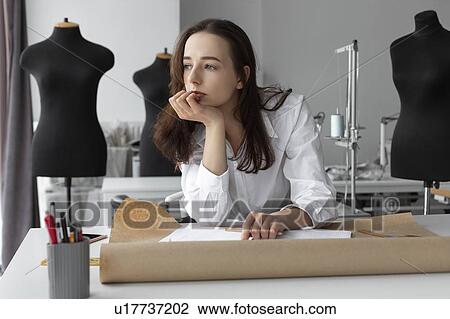 Stock Image - Fashion designer thinking at desk. Fotosearch