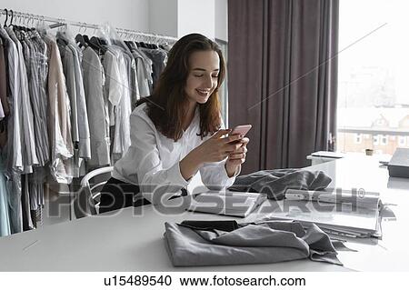 Stock Image - Fashion designer using smartphone in studio. Fotosearch