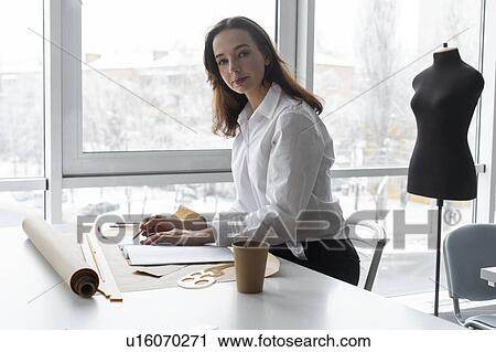 Stock Image - Fashion designer working at desk in studio. Fotosearch