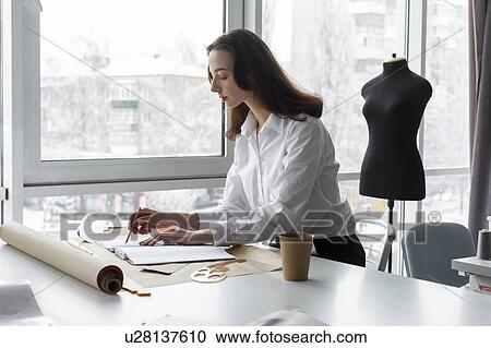 Stock Image - Fashion designer working at desk in studio. Fotosearch
