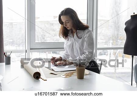 Stock Photo - Fashion designer working at desk in studio. Fotosearch
