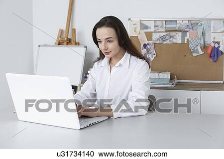 Stock Image - Fashion designer working at laptop. Fotosearch
