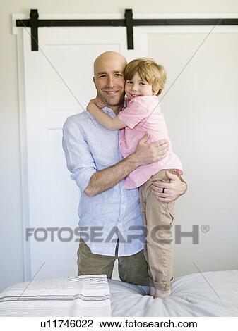 Stock Image - Father and son hugging in bedroom. Fotosearch