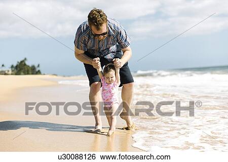 Stock Photograph - Father helping his baby girl walk on beach. Fotosearch