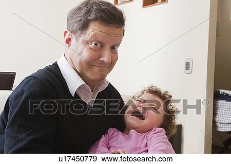 Stock Photo - Father making face while holding crying daughter. Fotosearch