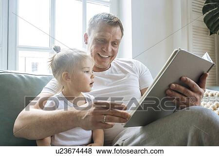 Father reading book to daughter on sofa View Large Photo Image Stock Photo - Father reading book to daughter on sofa. Fotosearch