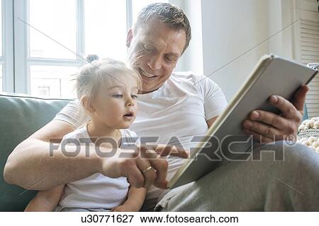 Stock Photo - Father reading book to daughter on sofa. Fotosearch