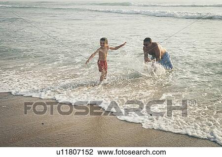 Stock Image - Father splashing son on beach. Fotosearch