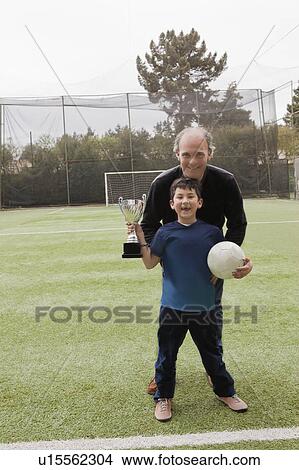 Picture - Father with his son holding soccer ball and trophy. Fotosearch
