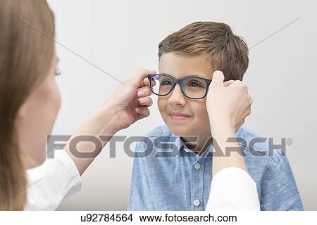 Female optician putting glasses on boy. View Large Photo Image Picture - Female optician putting glasses on boy.. Fotosearch