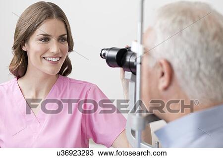 Stock Image - Female optician testing senior man's eyesight.. Fotosearch