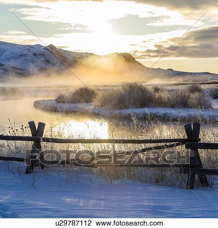 Stock Image - Fence by river at sunrise in Picabo, Idaho. Fotosearch
