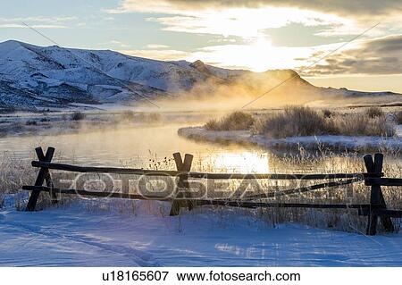 Stock Photo - Fence by river at sunrise in Picabo, Idaho. Fotosearch