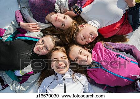 Stock Image - Five teenage girl skiers lying in a circle in snow, overhead portrait, Tyrol, Styria, Austria. Fotosearch