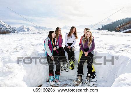 Stock Photography - Five teenage girl skiers sitting laughing in snow covered landscape, Tyrol, Styria, Austria. Fotosearch