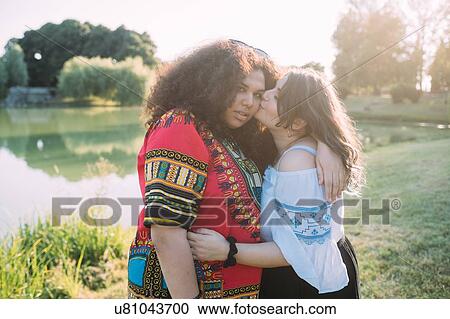 Friends hugging and kissing on cheek in park View Large Photo Image Stock Image - Friends hugging and kissing on cheek in park. Fotosearch