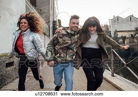 Stock Image - Friends laughing and playing by river, Milano, Lombardia, Italy. Fotosearch