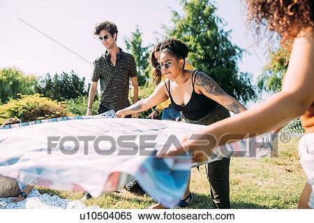 Stock Photography - Friends laying picnic blanket in park. Fotosearch