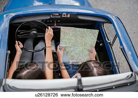 Stock Photograph - Friends reading route map inside car. Fotosearch